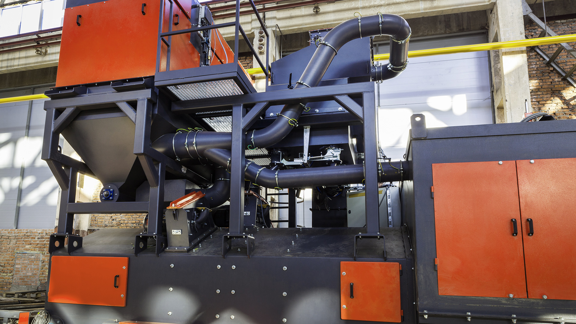 Industriemaschine mit schwarzen Rohren und roten Wänden in Fabrikumgebung.